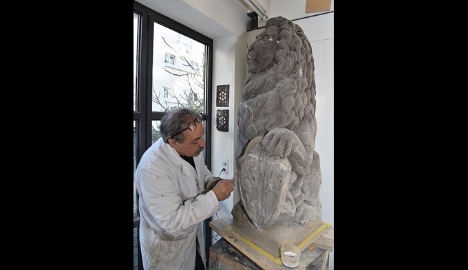 Bildhauer Vitus Wey bessert die wieder zutage getretenen Schäden am Sandstein-Löwen von Paul Amlehn aus. (Foto Daniel Zumbühl)