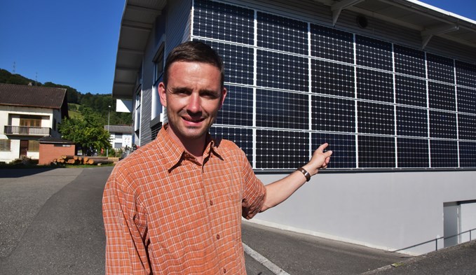 Der Trienger Gemeinderat Daniel Schmid zeigt eine der Solaranlagen in der Gemeinde: Die Fassade der Frey Electric AG.  (Foto Thomas Stillhart)