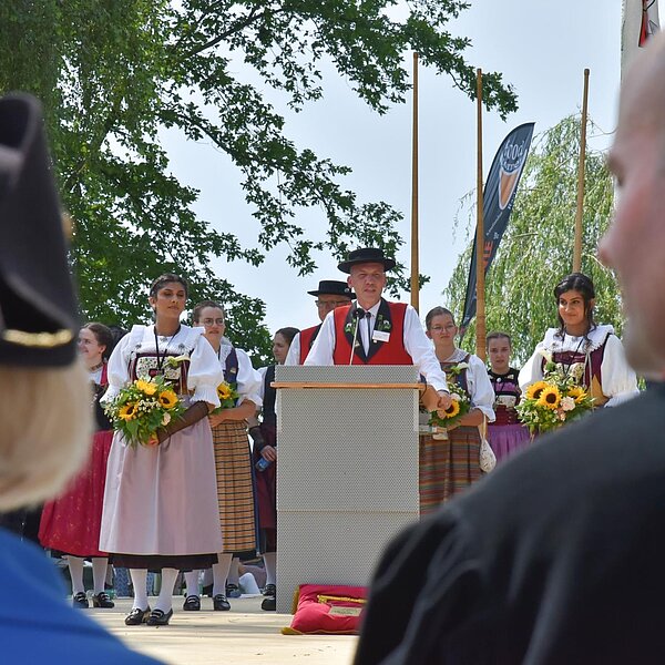 
									Adi Schöpfer, Präsident des Jodelclubs Sempach, ergreift an der Eröffnungsfeier das Wort. Im Vordergrund Standesweibelin Anita Imfeld-Müller und Regierungspräsident Fabian Peter. Bild: Foto Franziska Kaufmann
								